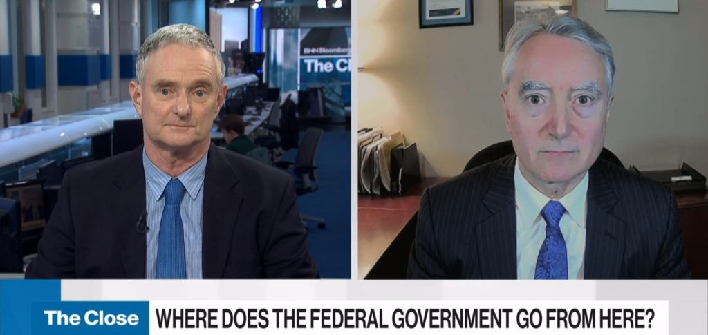 Two men on television, each looking straight to camera.