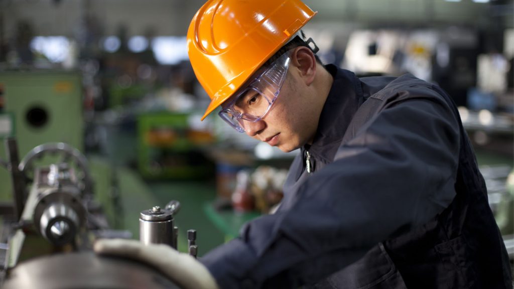 Man in hard hat and overalls working at a machine in a factory.